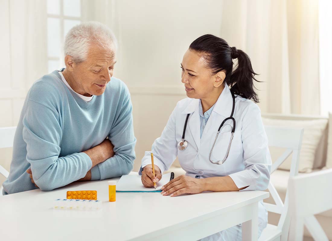 Medicare Part D - Smiling and Encouraging Doctor Takes Notes as She Discusses Medication Precautions and Side Effects with a Senior Male Patient in His Home at the Kitchen Table