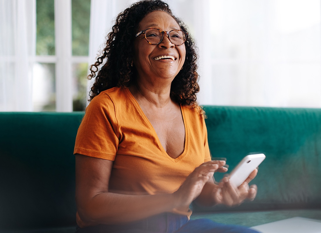 Report a Claim - Portrait of a Smiling Senior Woman Sitting on the Sofa at Home While Holding a Phone in her Hands