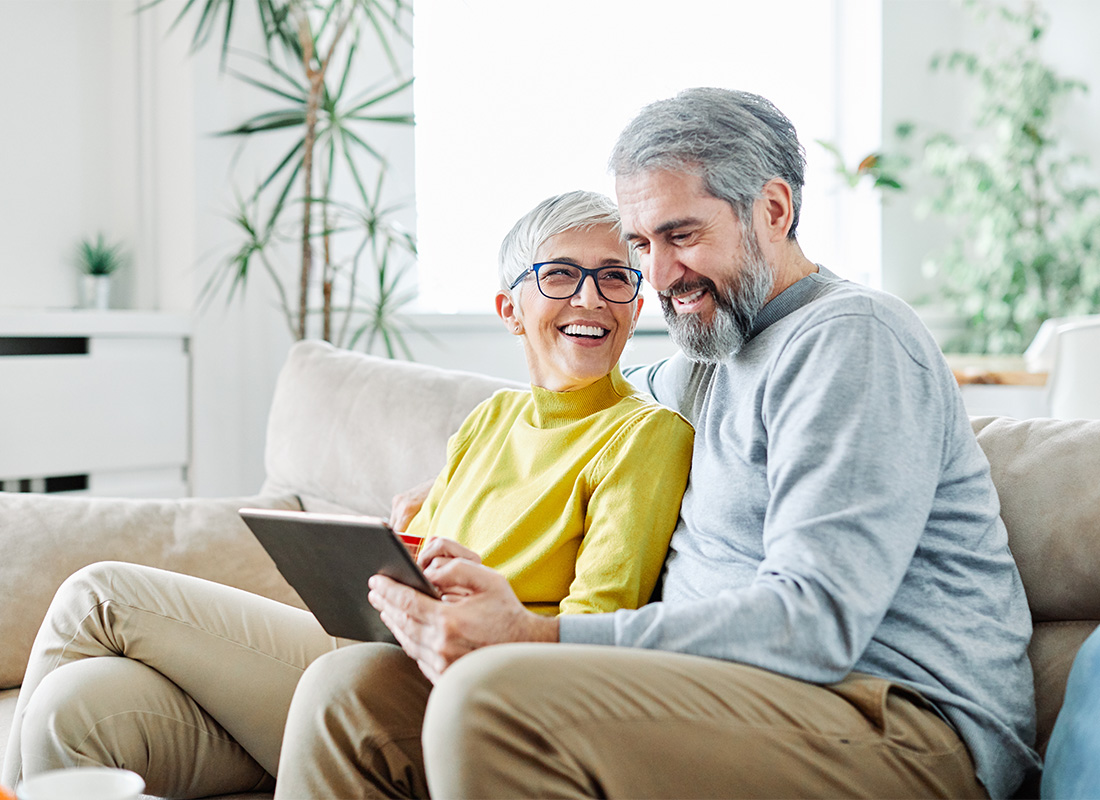 Blog - Portrait of a Cheerful Elderly Couple Sitting on the Sofa on a Sunny Morning While Using a Tablet Together